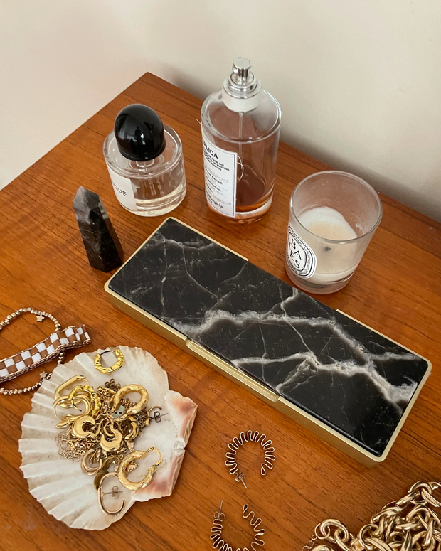 Tabletop scene with jewellery, a candle, and a tray on a wooden surface.