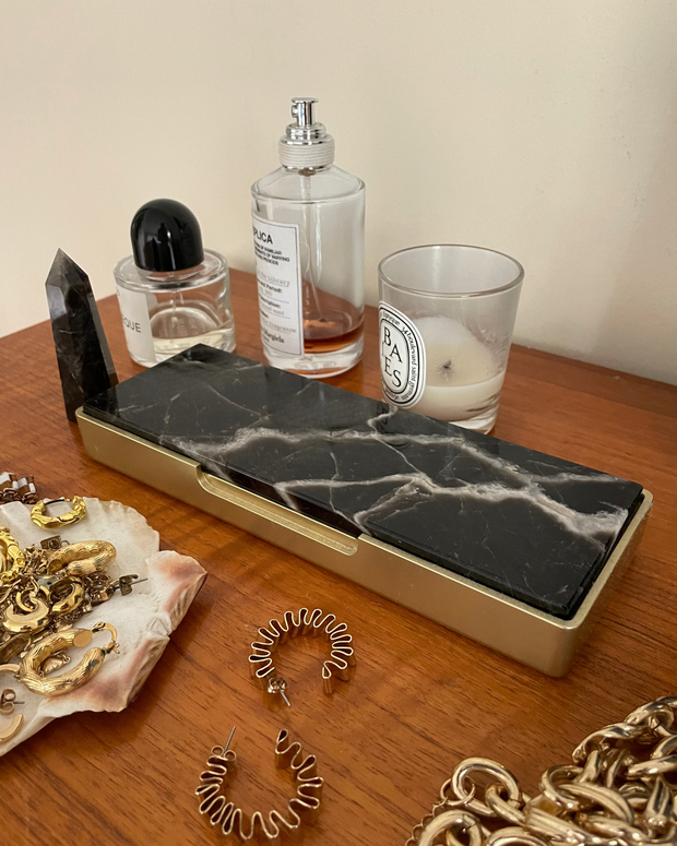 Marble-patterned homewares for jewellery storage on a wooden surface with jewelry and a candle next to it.